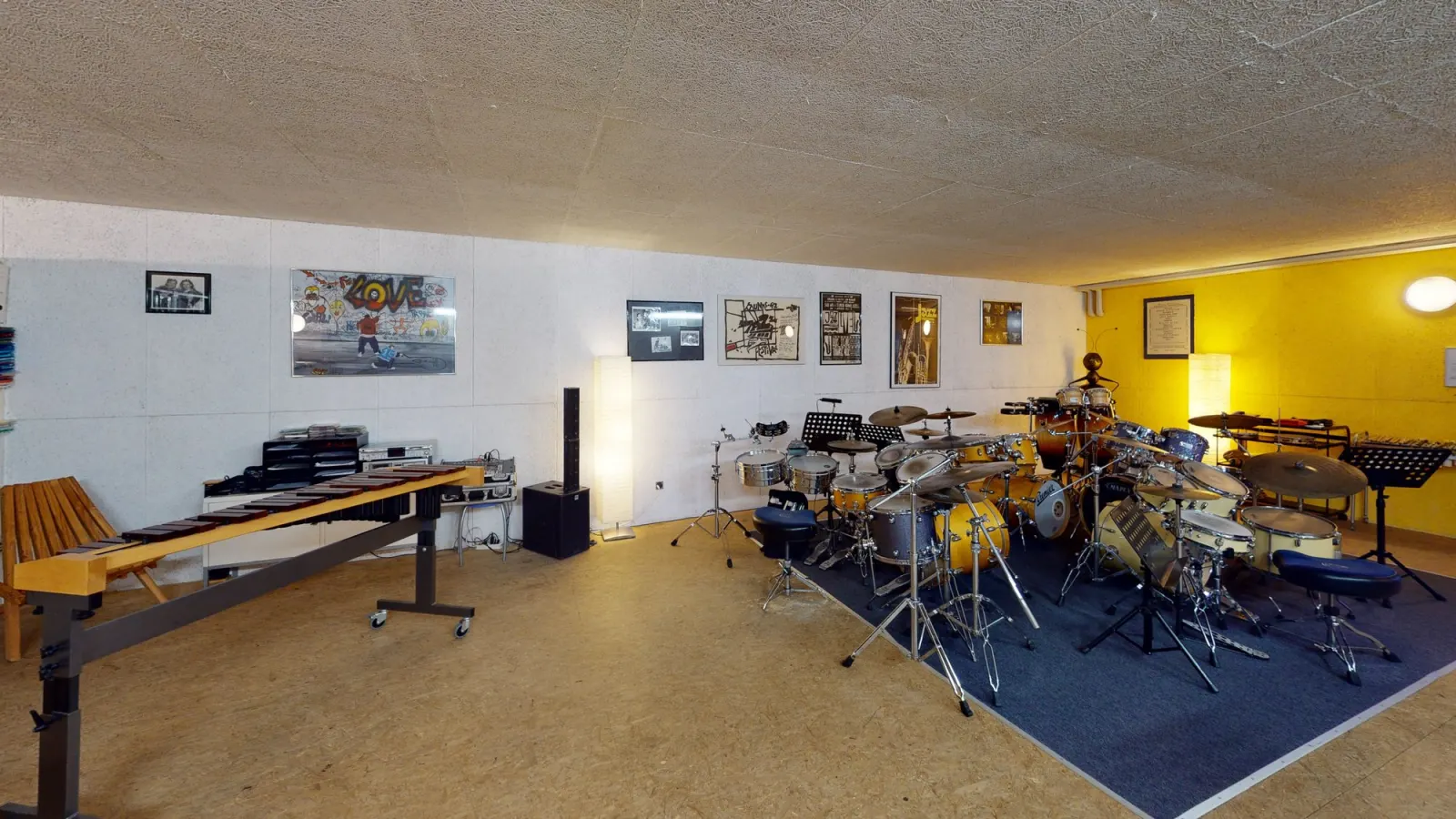 Sala con batteria e strumenti davanti a una parete gialla, tour 12